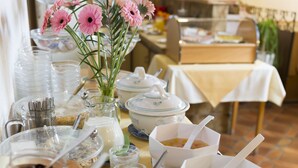 A buffet table with various food items and a vase of pink flowers. - Hotel Dreisonnenberg (Neuschoenau)