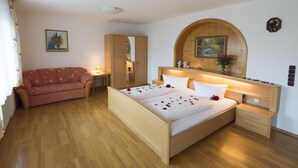 A bedroom with a wooden bed, a wooden wardrobe, a wooden nightstand, a wooden arched mirror, and a wooden headboard. - Hotel Dreisonnenberg (Neuschoenau)