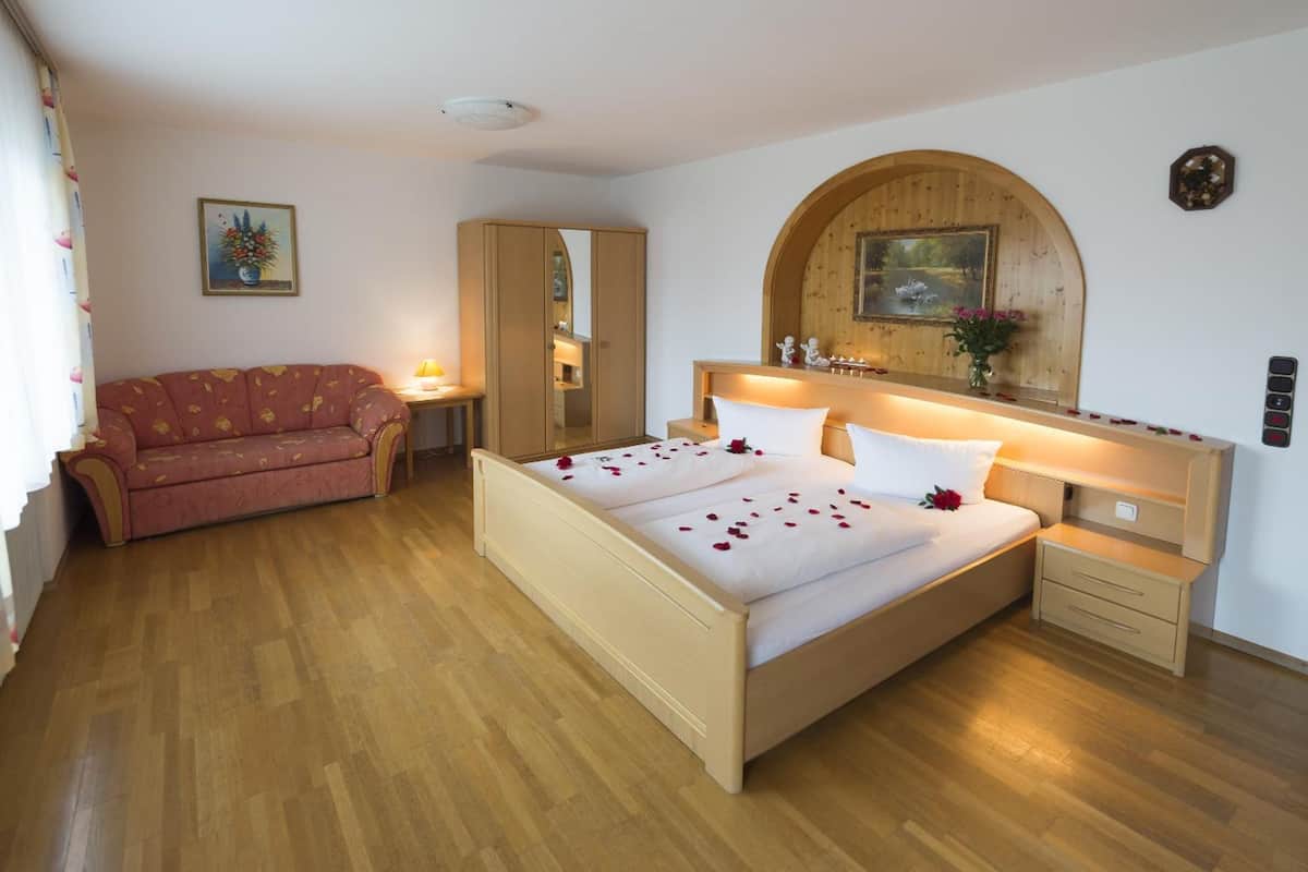 A bedroom with a wooden bed, a wooden wardrobe, a wooden nightstand, a wooden arched mirror, and a wooden headboard.