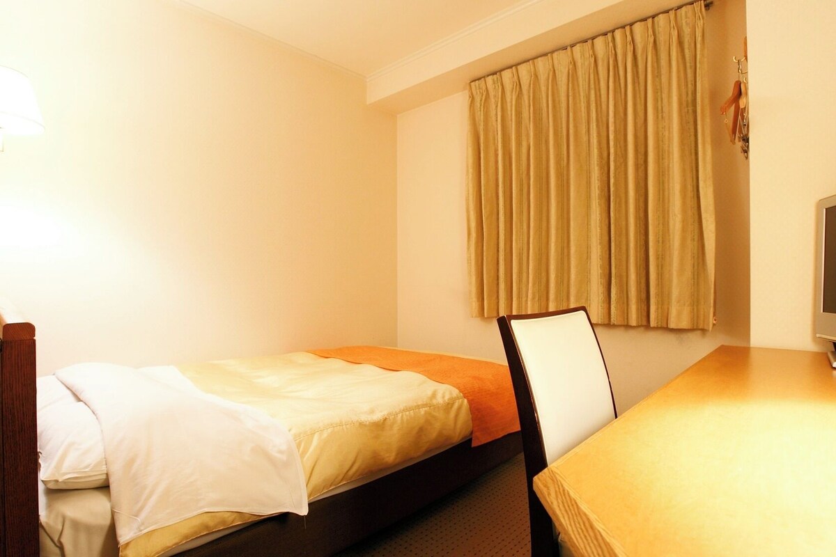 A hotel room with a bed, a desk, a television, and a window with curtains.