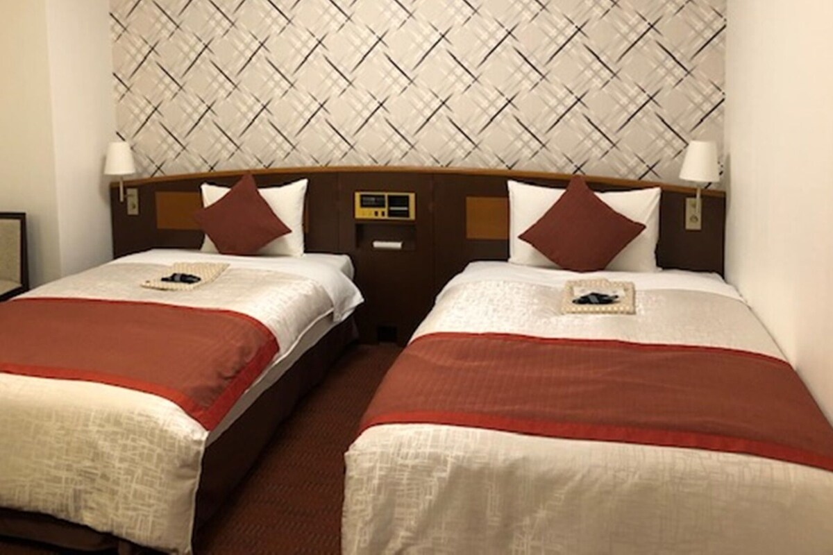 A hotel room with two beds, a small table, and a headboard with a patterned design.