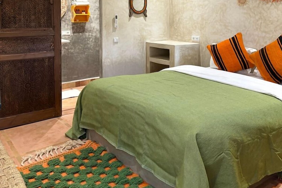 Un dormitorio con cama, mesita de noche, espejo en la pared y puerta con diseños elaborados.