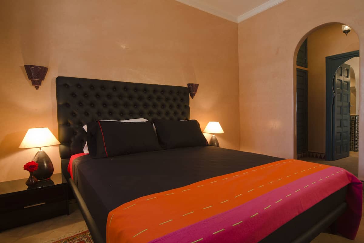 Una cama con cabecera capitonada, dos lámparas de noche y una rosa decorativa.