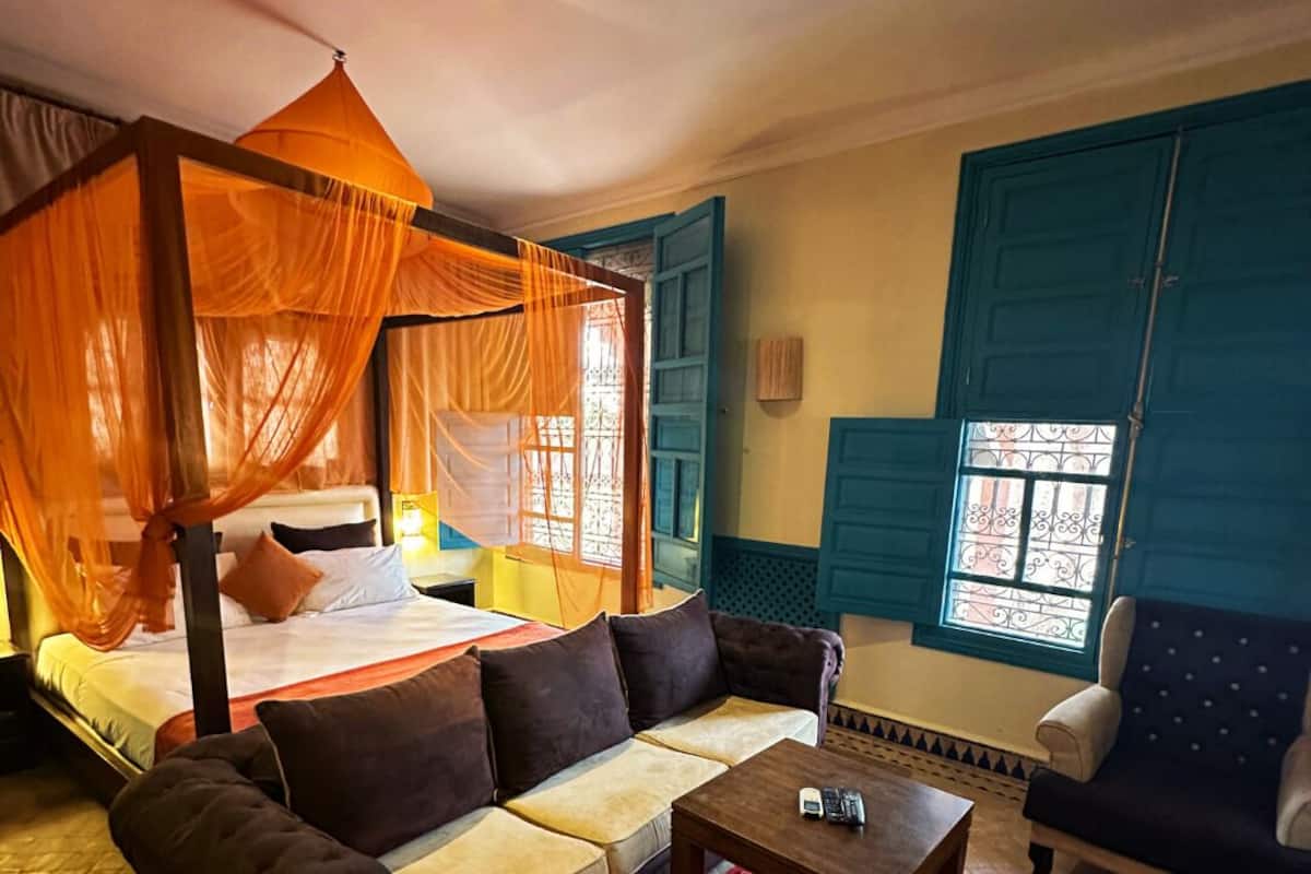 Una habitación con una cama con dosel, un sofá, una mesita de centro y una ventana con contraventanas azules.