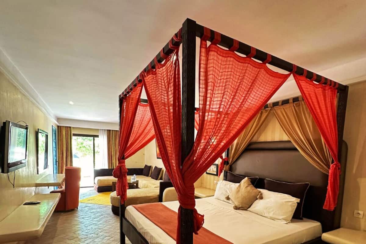 Una cama con dosel y mosquitera roja, un tapete rojo y un televisor sobre un mueble.