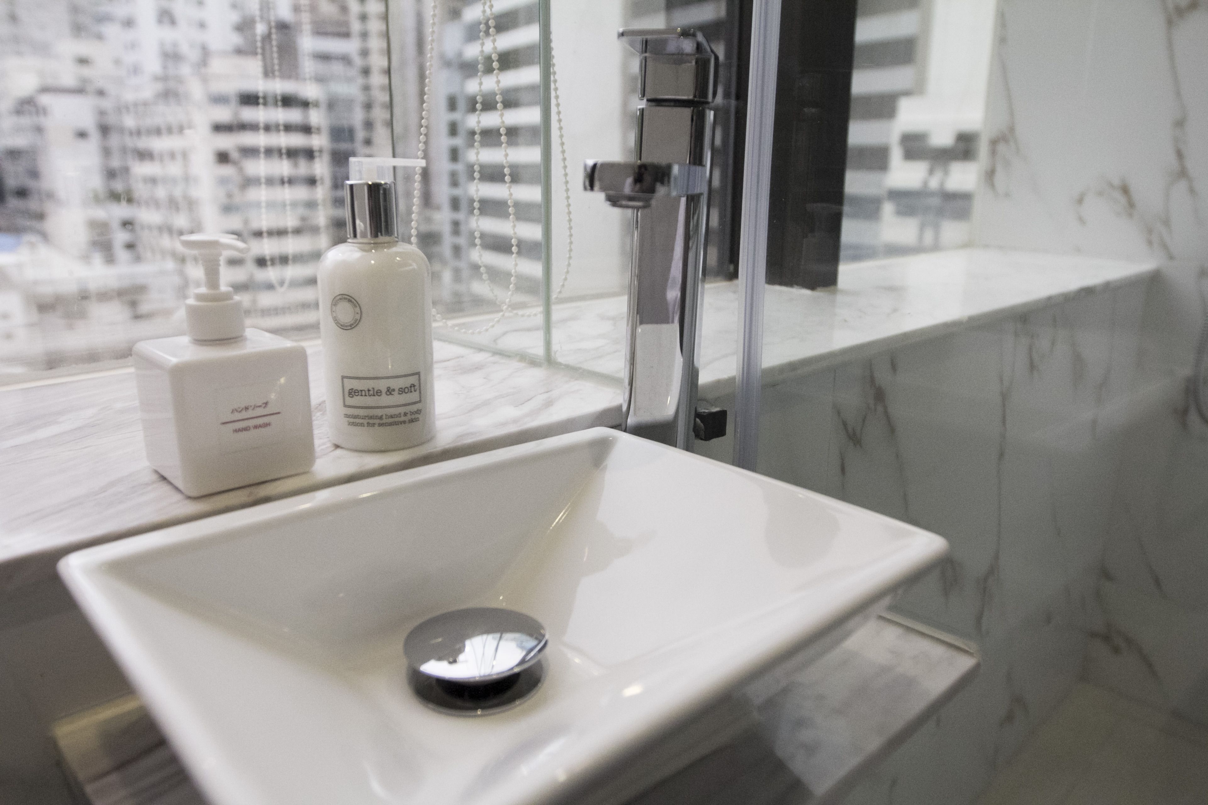 A bathroom with a white sink, a handheld showerhead, and a bottle of hand soap.