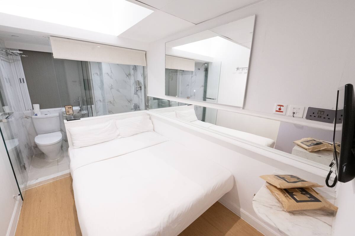 A modern hotel room with a large bed, a glass shower enclosure, a toilet, and a large mirror.