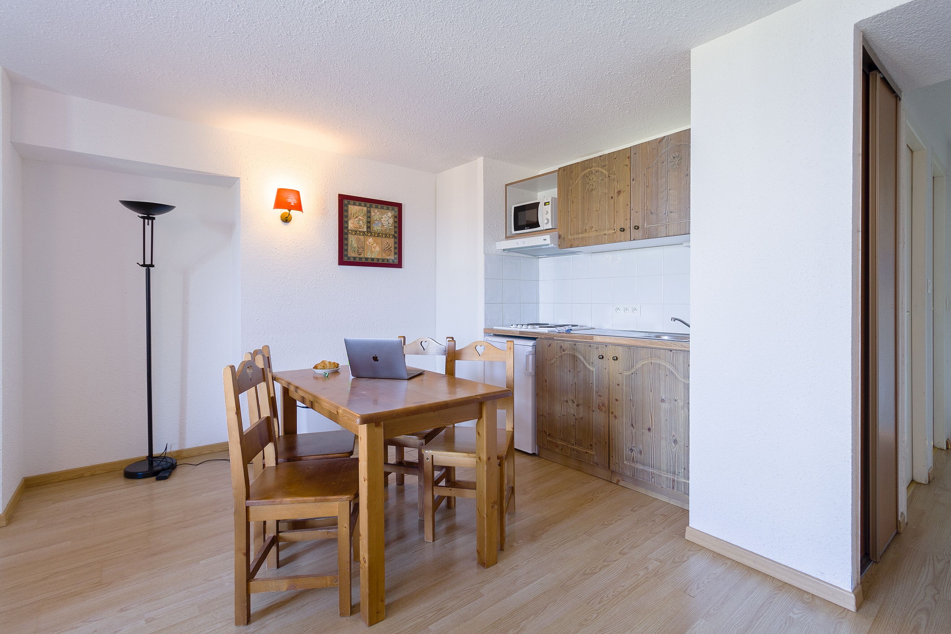 A compact kitchen with wooden cabinets, a microwave, and a dining area with a table and chairs.