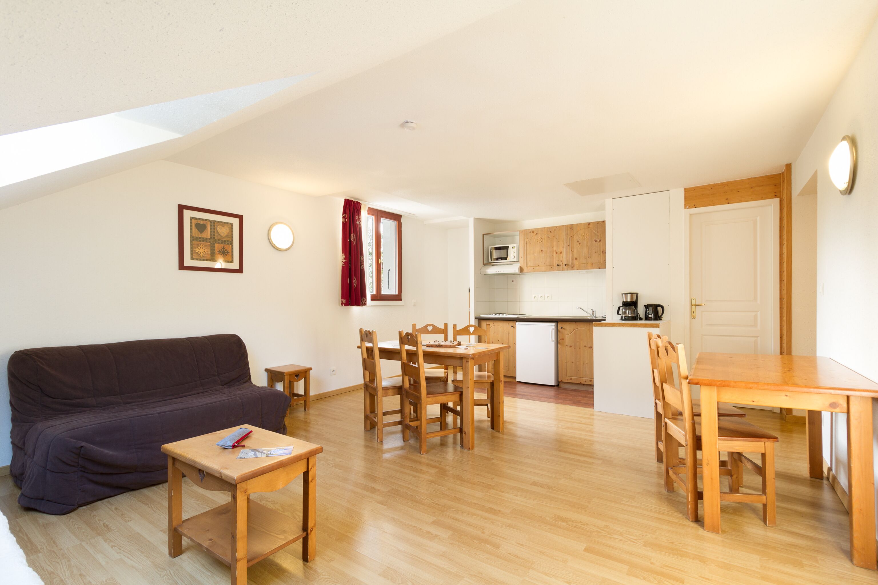A compact living space with a sofa, dining table, chairs, a small kitchen area, and a ceiling with skylight.