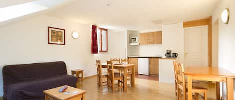 A compact living space with a sofa, dining table, chairs, a small kitchen area, and a ceiling with skylight.