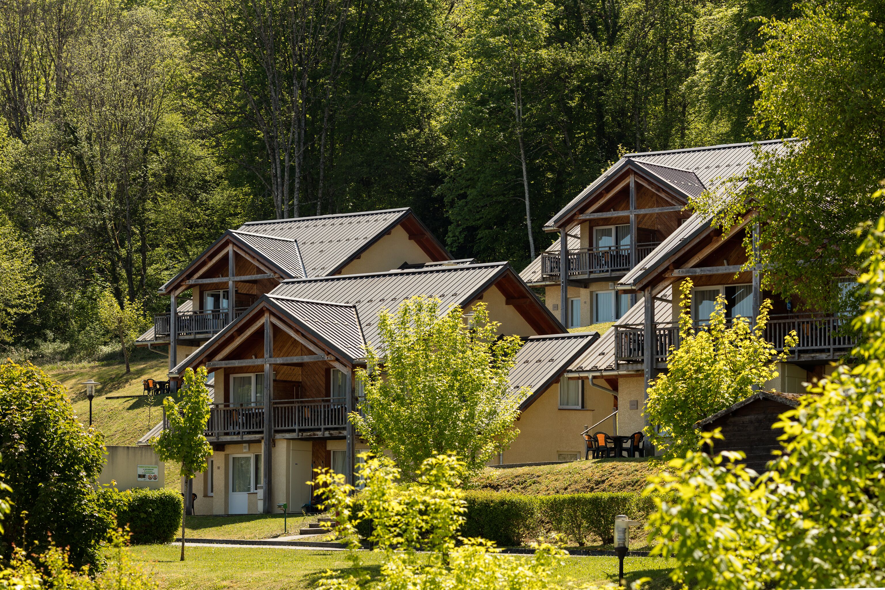 A row of wooden cabins with balconies, surrounded by lush greenery and trees.