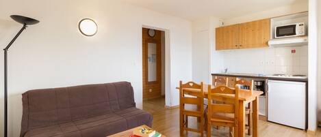 A compact living space with a sofa, a dining table with chairs, a small kitchen area with a microwave, and a floor lamp.