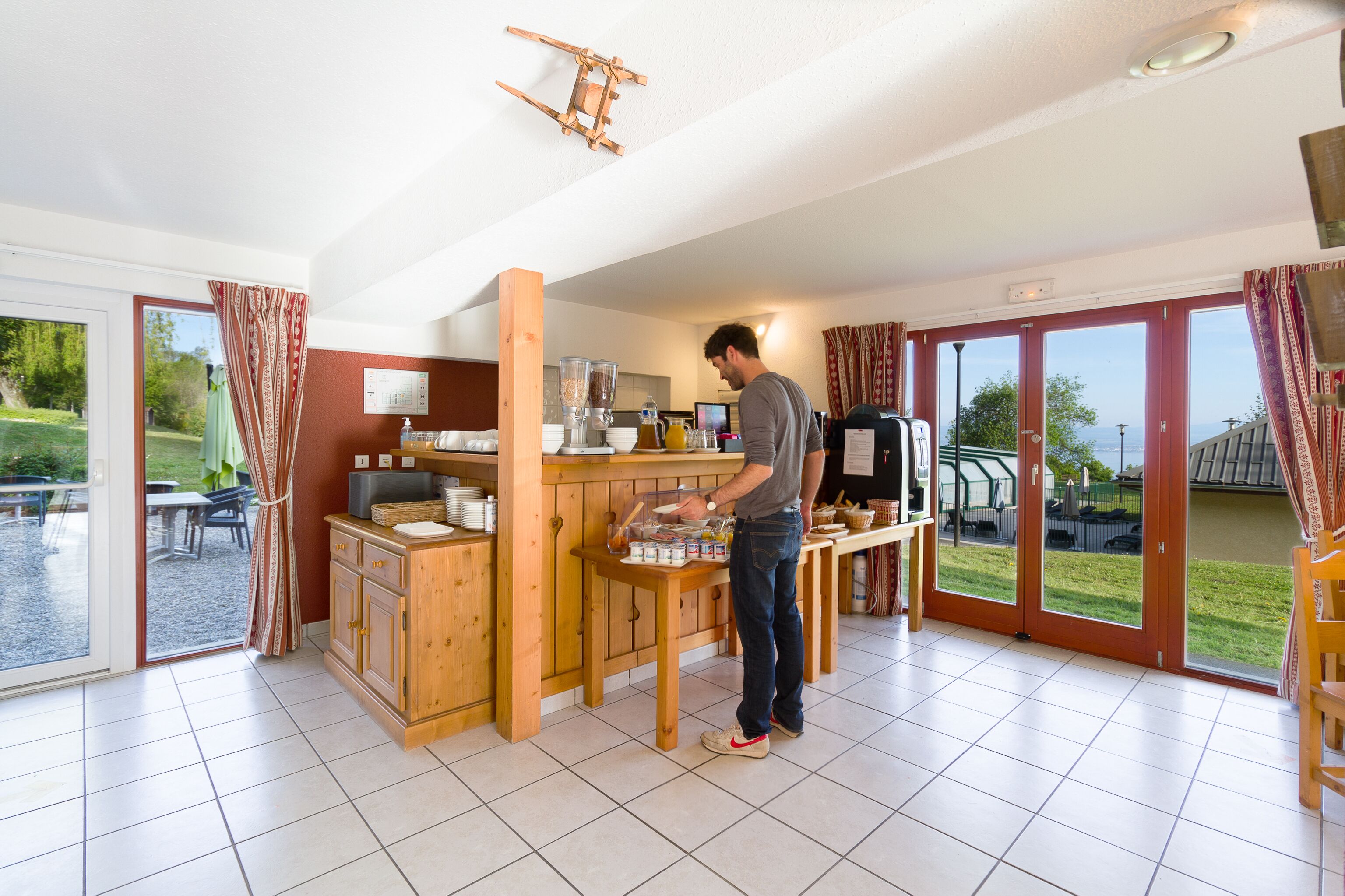 Une cuisine avec un comptoir en bois, un homme qui prépare des aliments et une vue sur l’extérieur grâce à de grandes portes-fenêtres coulissantes.