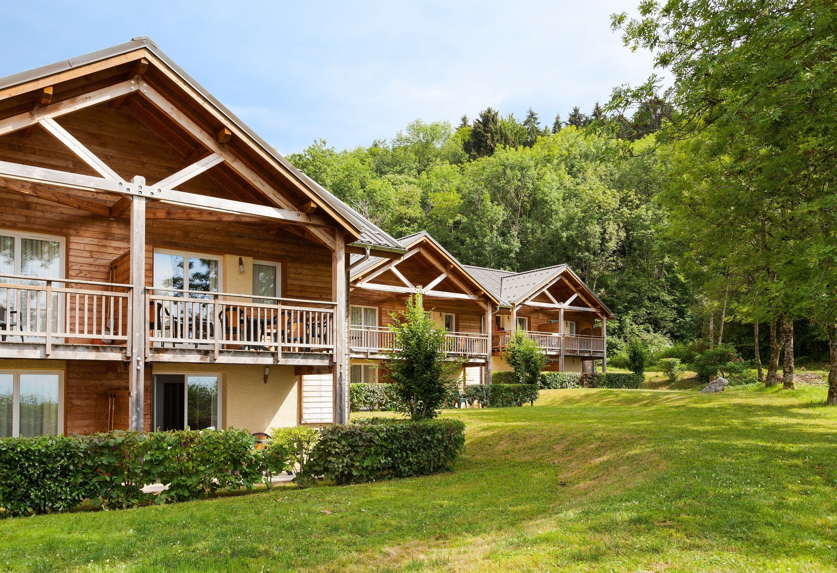 A row of log cabin-style cabins with balconies, surrounded by lush greenery and trees.