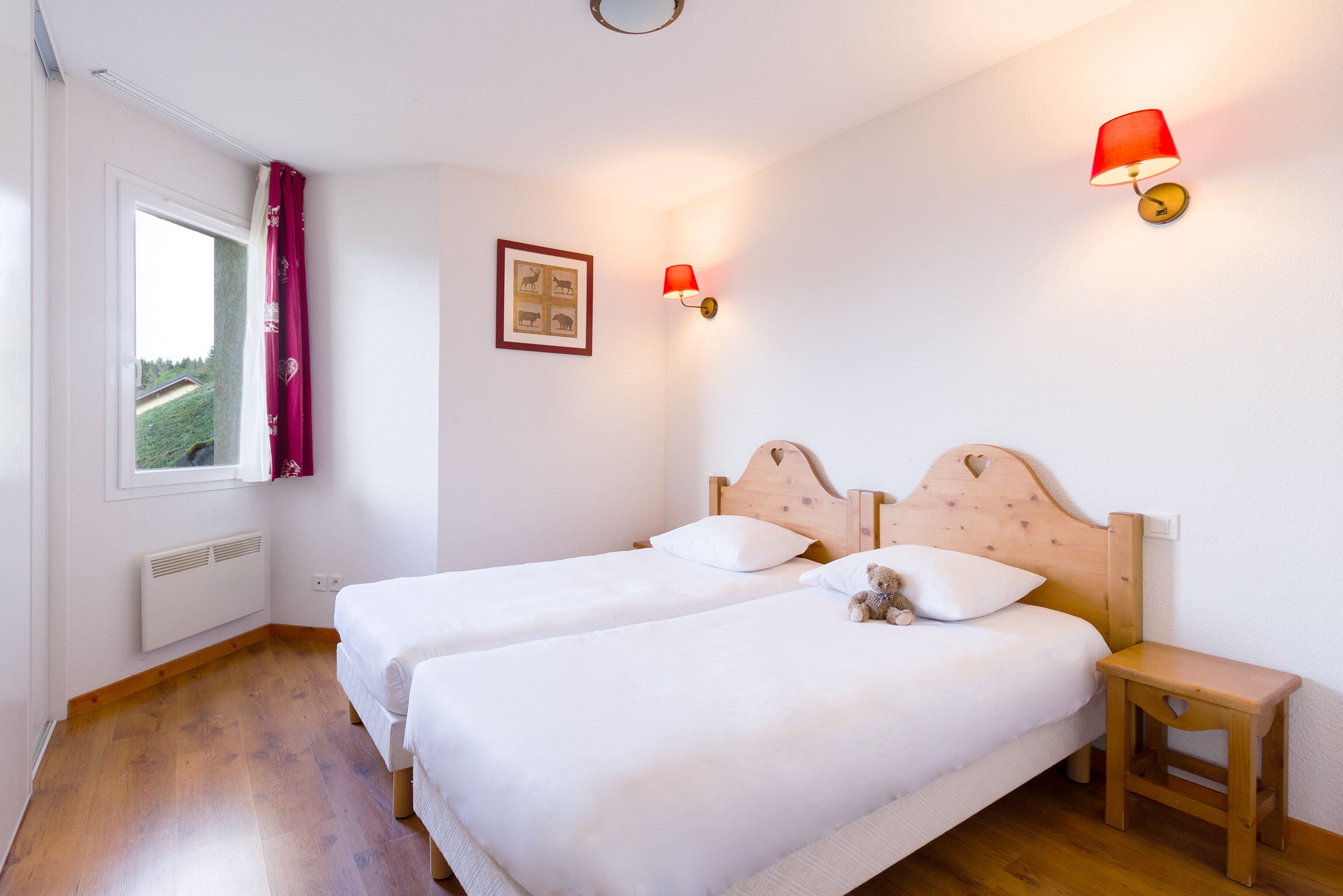 Een slaapkamer met twee eenpersoonsbedden, een klein nachtkastje, een raam met uitzicht en een wandlamp.