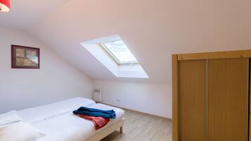 Een slaapkamer met dakraam, een bed, een houten kledingkast en een ingelijst schilderij aan de muur.