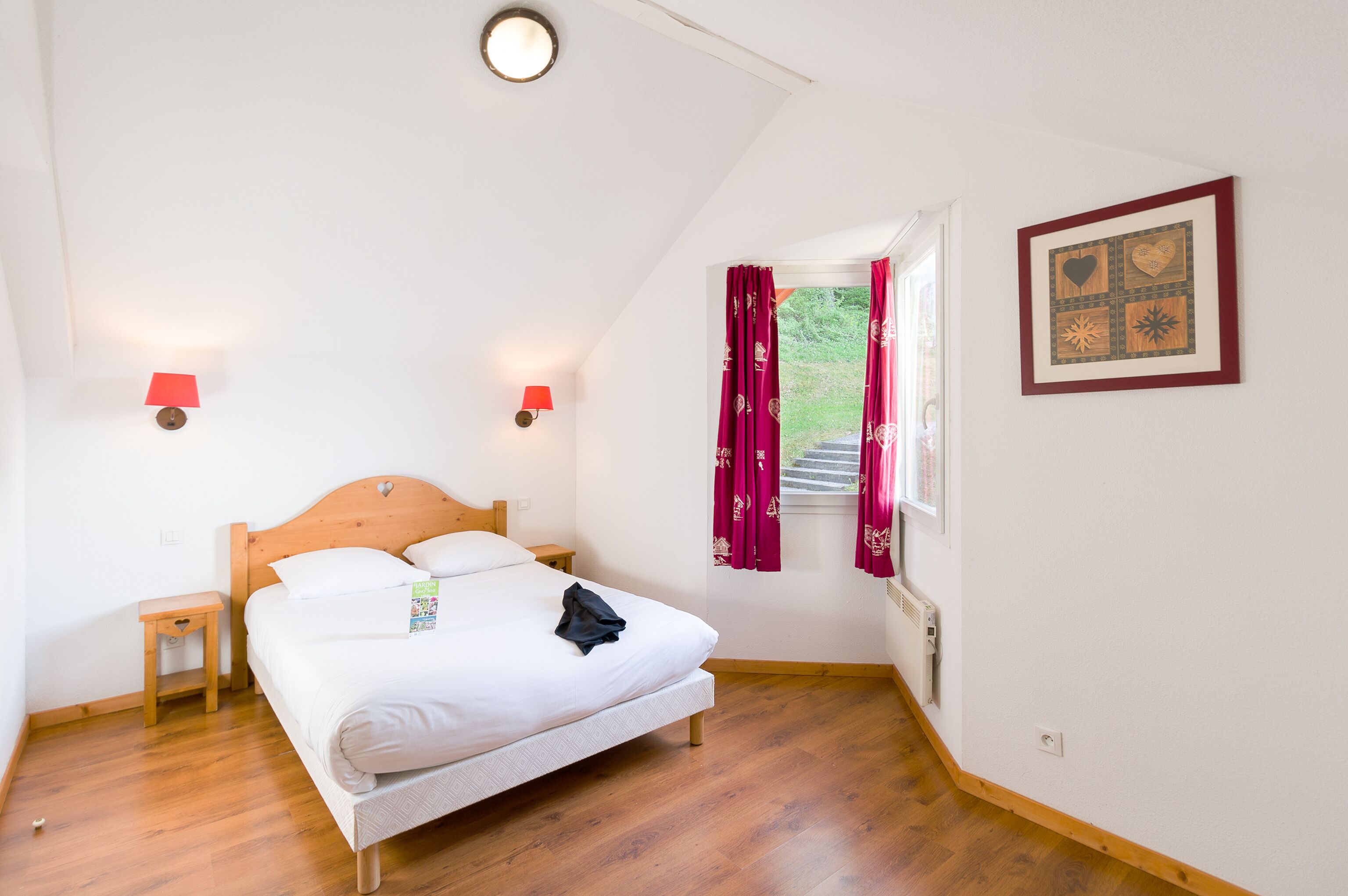 A bedroom with a wooden bed, two bedside tables, a window with curtains, and a wall-mounted picture.