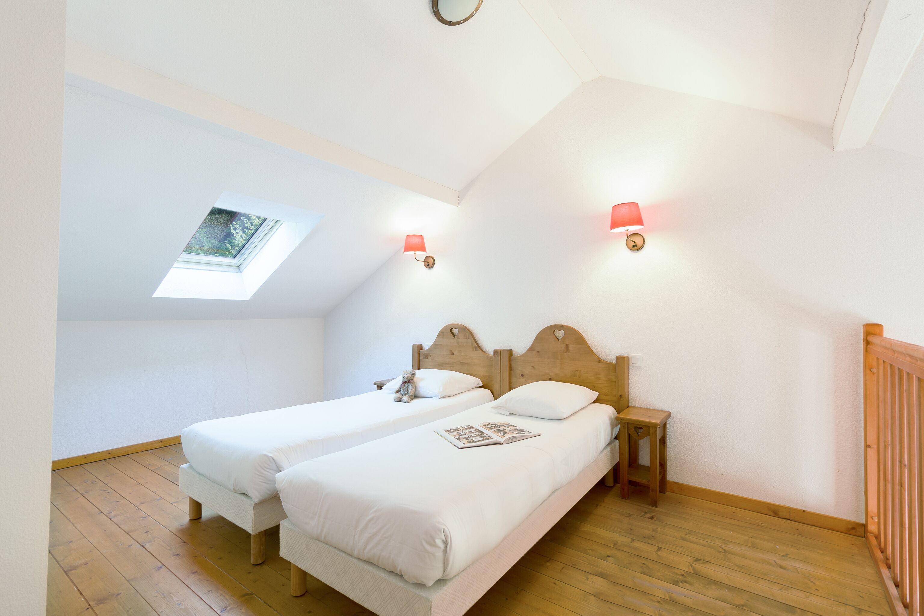 Een slaapkamer met twee enkele bedden, een dakraam en twee wandlampen.