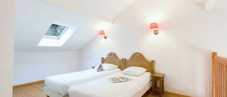 A bedroom with two single beds, a skylight, and two wall-mounted lamps.
