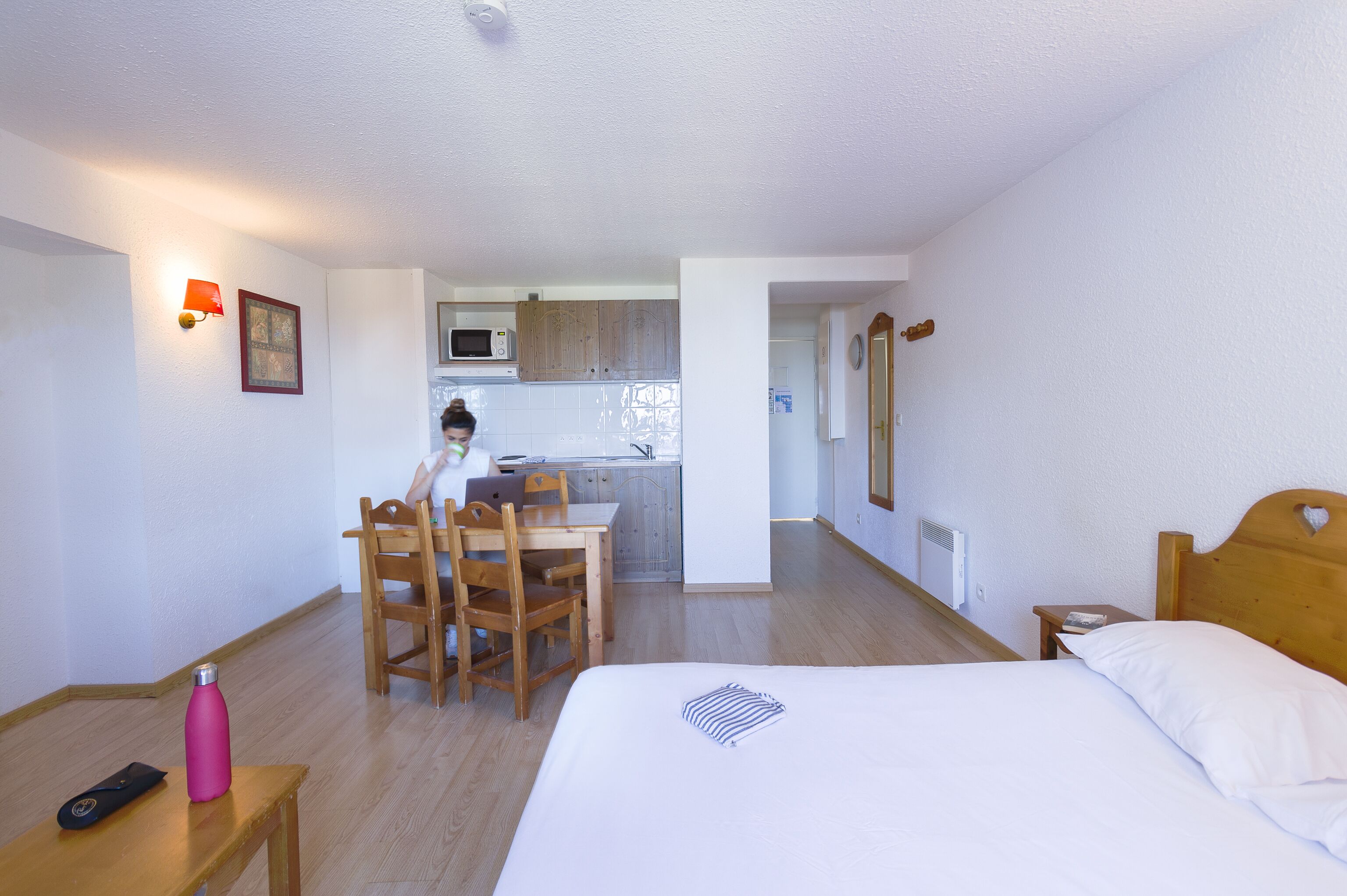 Ein Hotelzimmer mit einem Bett, einem Schreibtisch, einem Stuhl, einem kleinen Tisch und einer Küchenzeile im Hintergrund.