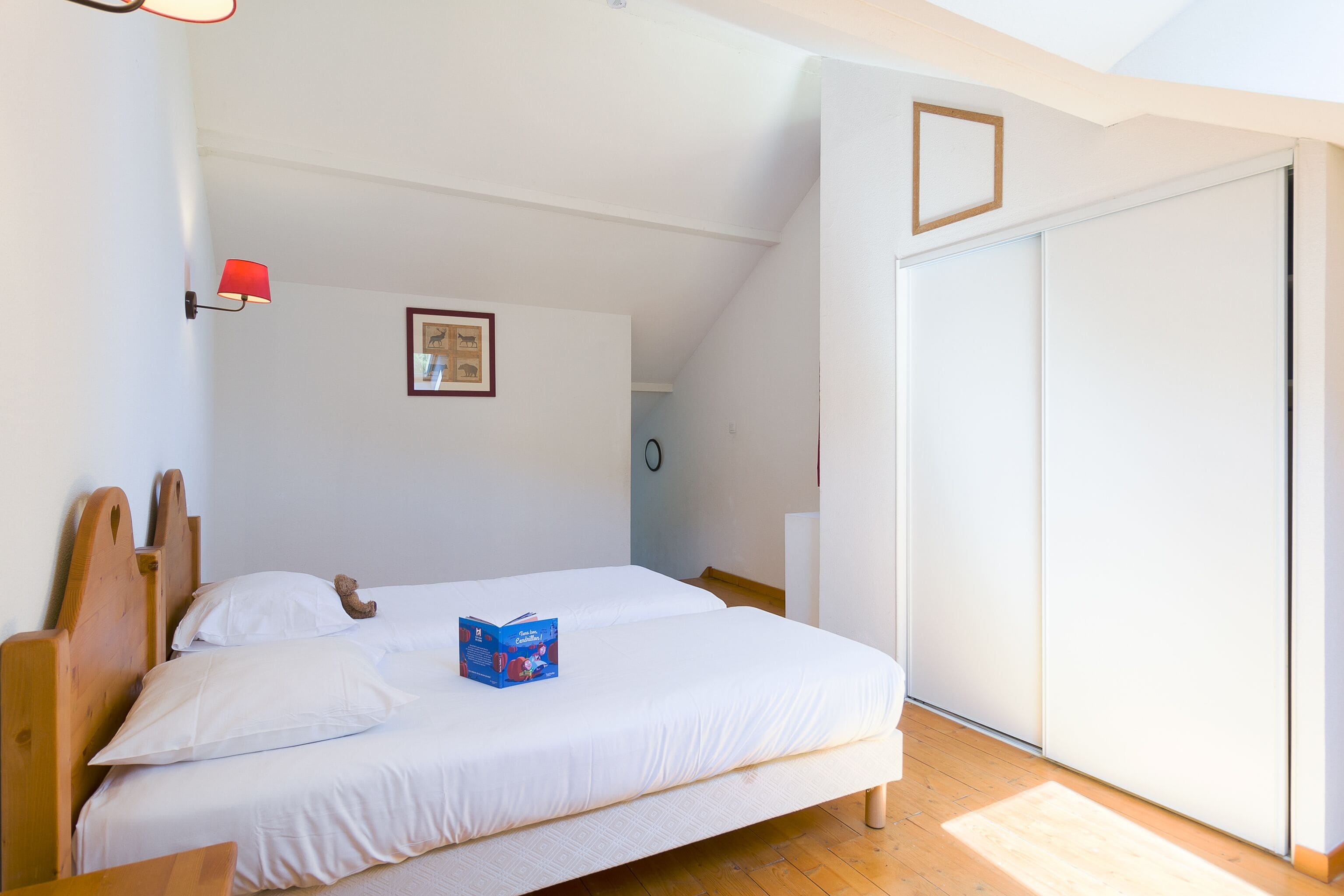 A bedroom with two single beds, a red wall lamp, a framed picture, and a sliding door.