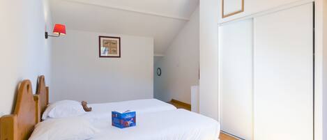 A bedroom with two single beds, a red wall lamp, a framed picture, and a sliding door.
