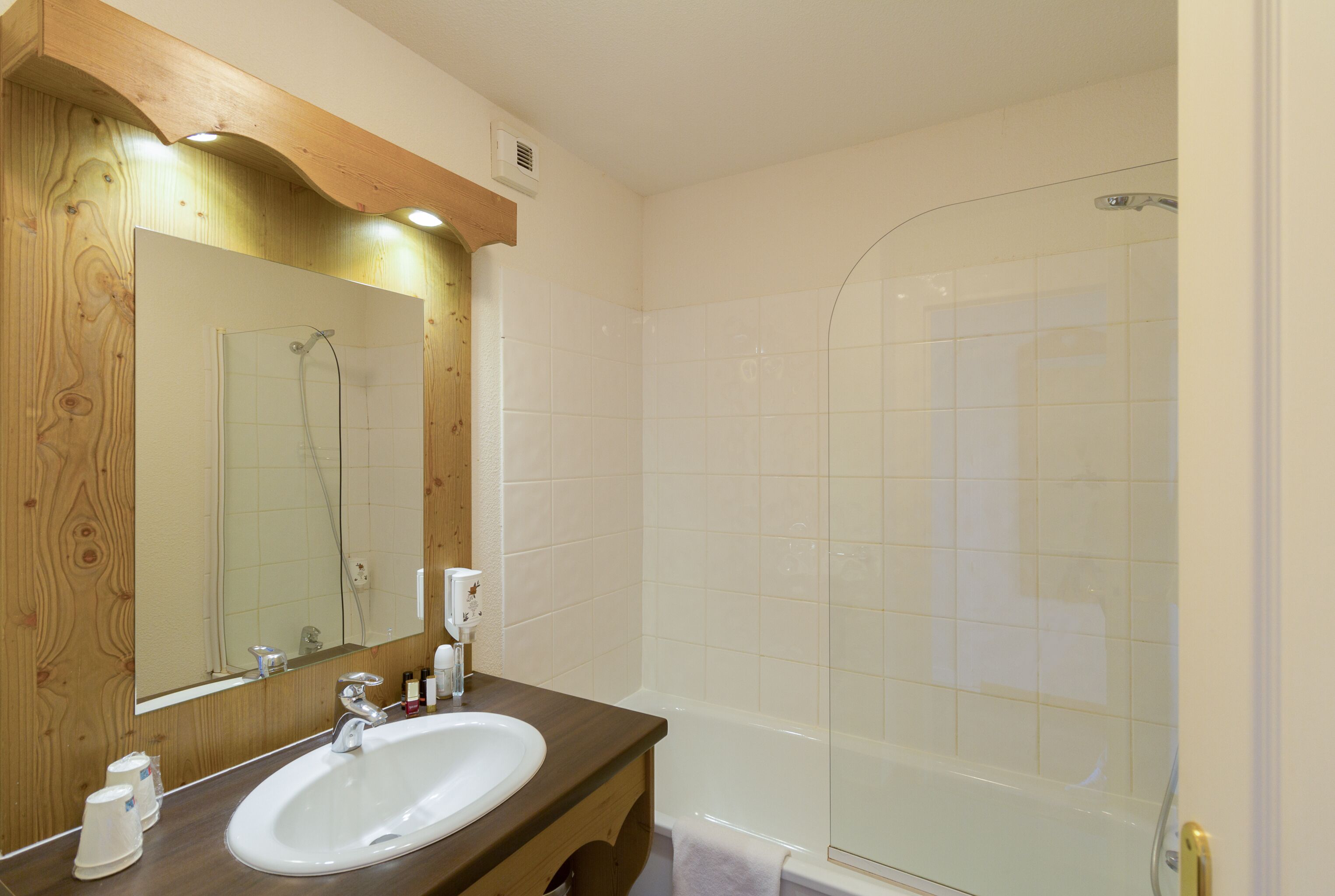 Een badkamer met een houten wastafelmeubel, een wastafel, een spiegel en een douche met glazen wanden.