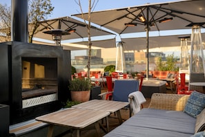 Une terrasse extérieure dotée d’un poêle à bois, de chaises rouges et blanches, et de parasols pour créer de l’ombre.
