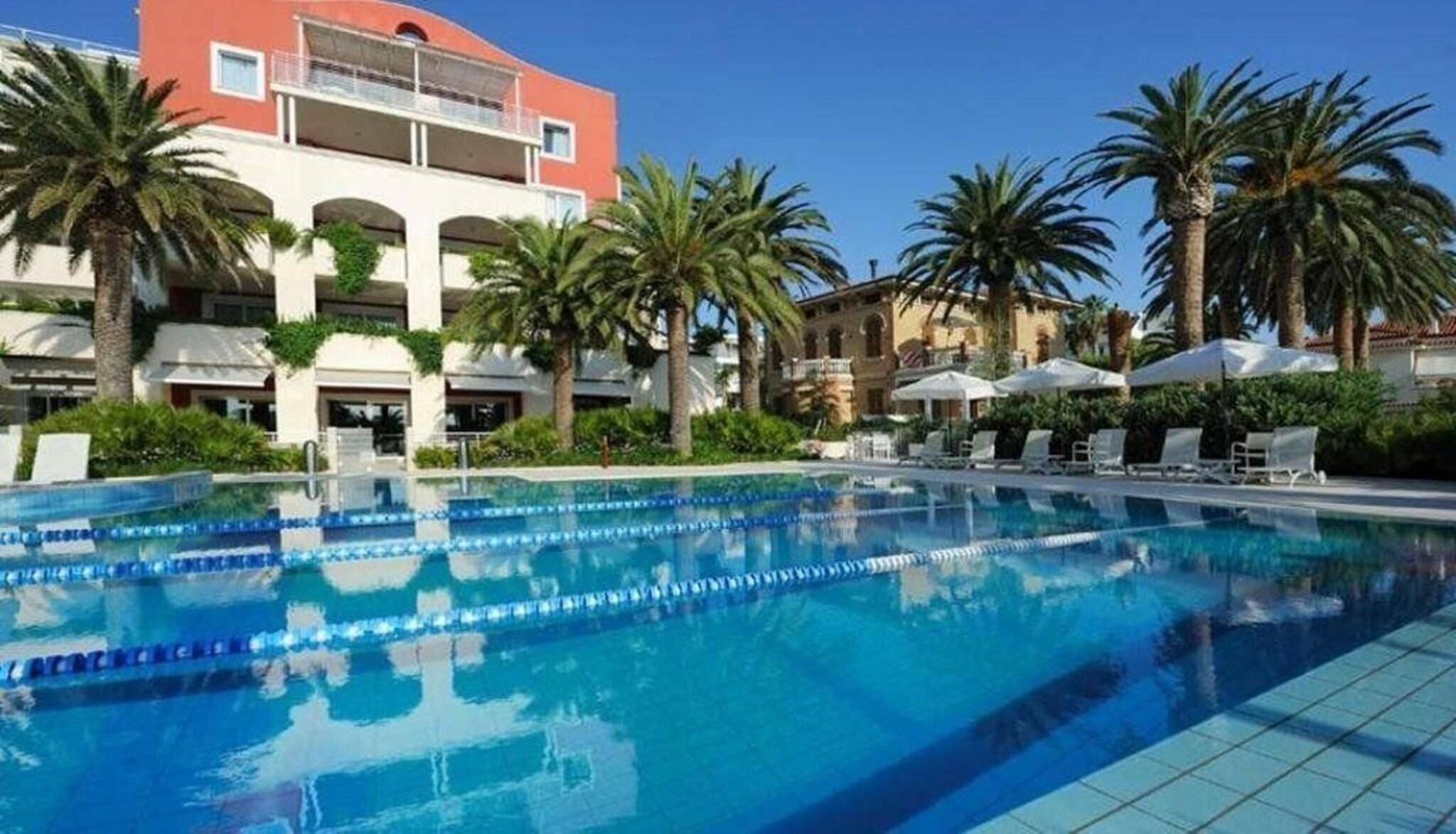 Une piscine à l’eau d’un bleu cristallin, entourée de palmiers et bordée d’un bâtiment doté de balcons.