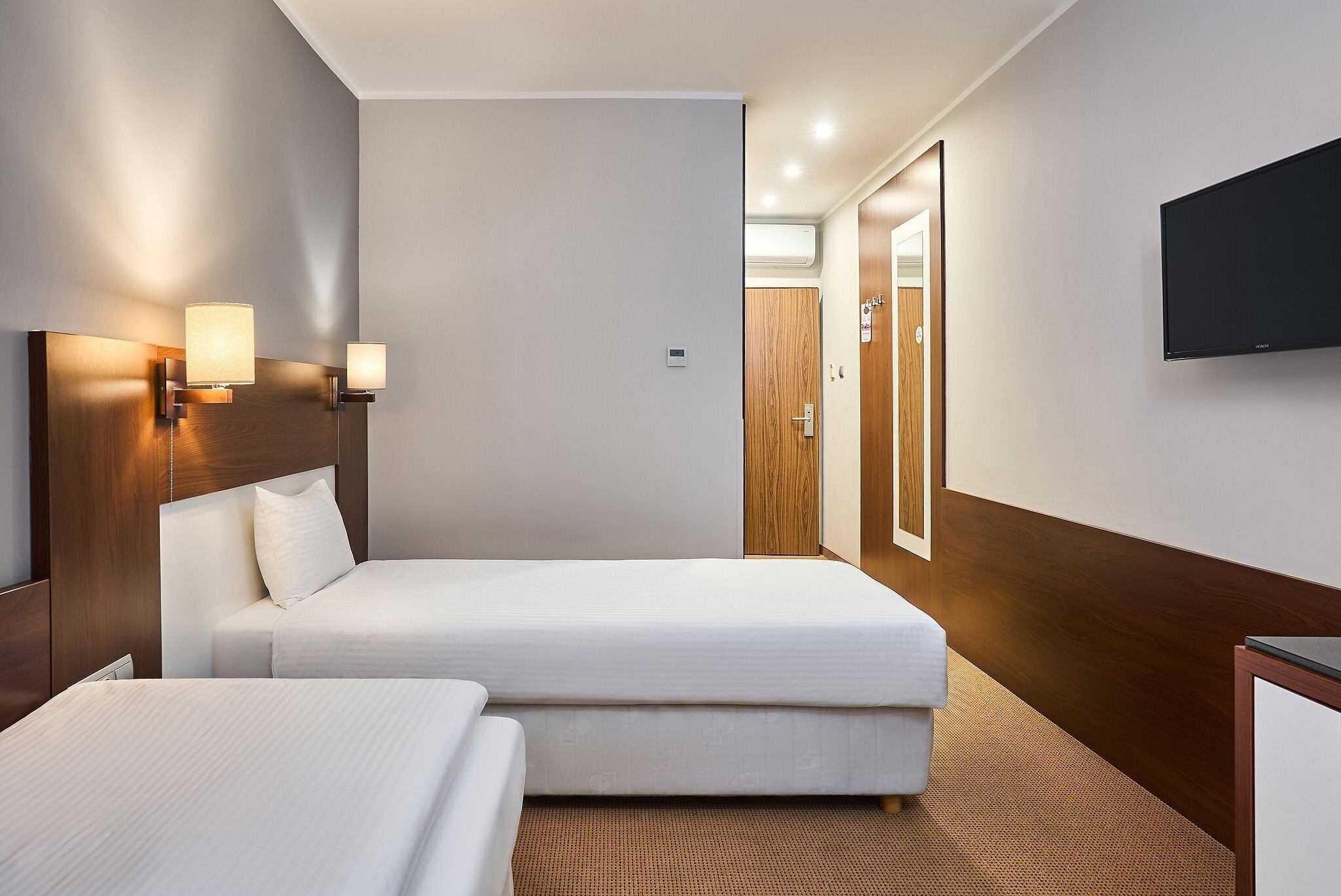 Habitación de hotel con dos camas, un televisor de pantalla plana, luces empotradas en la pared y un cabecero de madera.