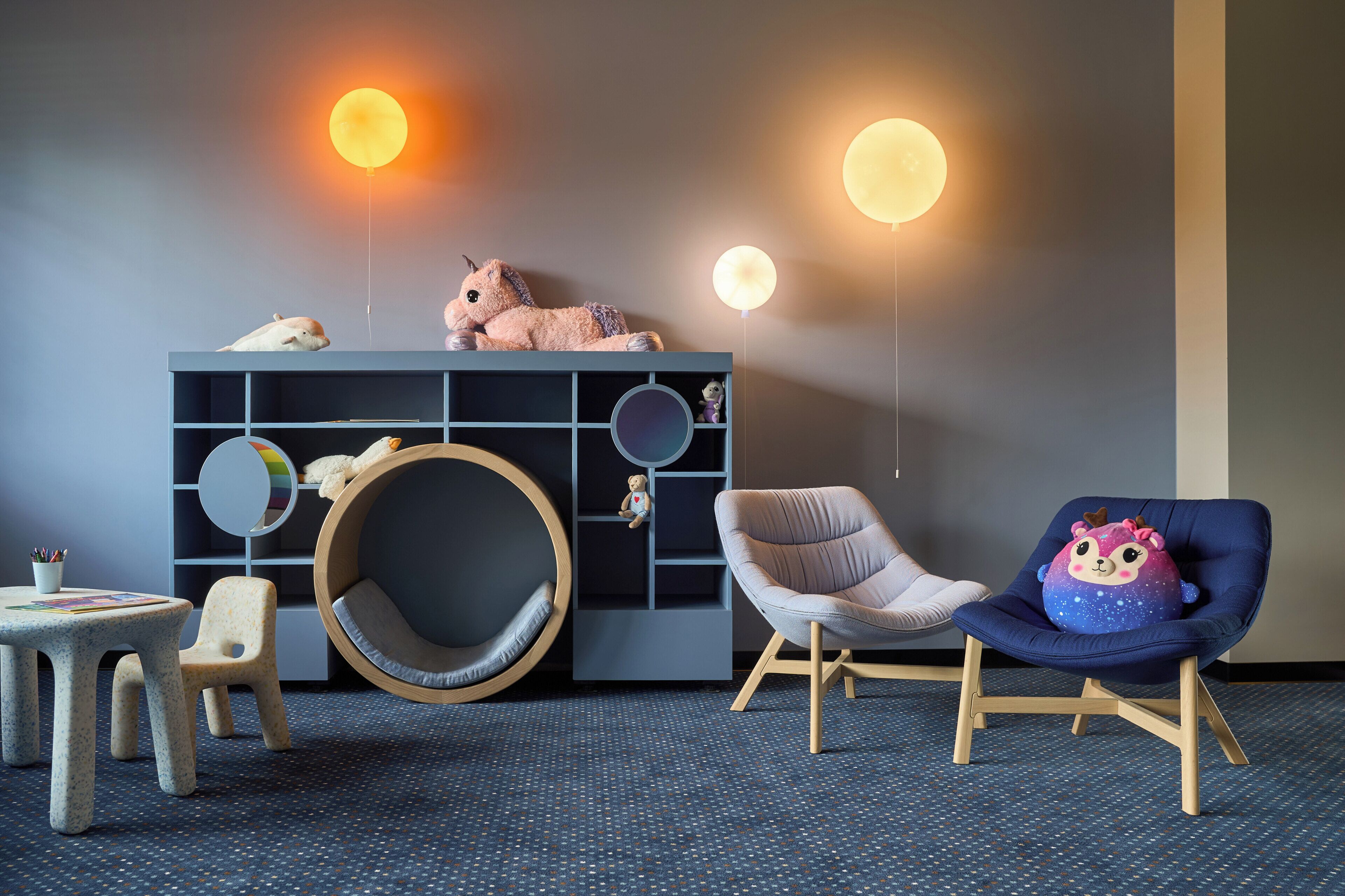 A room with a round seating area, a blue chair, a small table, and a dark-colored cabinet with shelves.