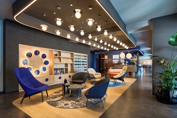 A modern lobby with multiple seating areas, a reception desk, and a variety of decorative wall elements. - DeSilva Inn Katowice Airport (Ozarowice)