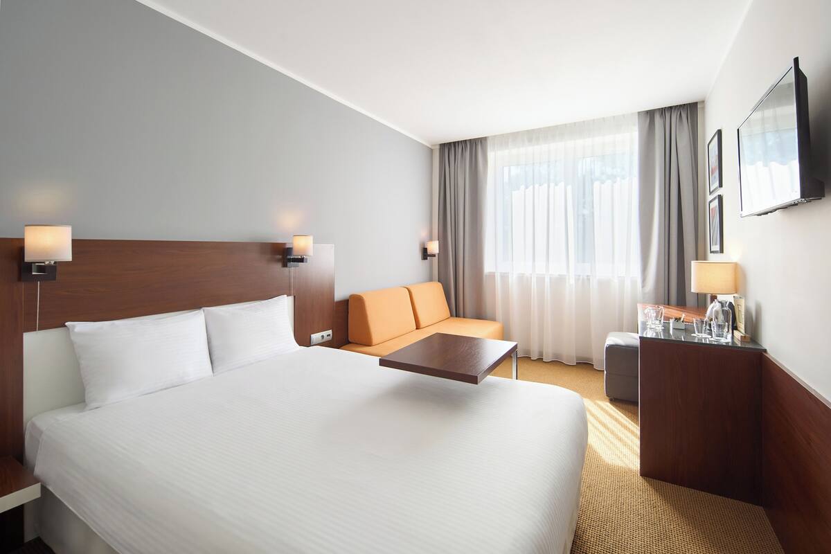 A hotel room with a large bed, a sofa, a desk, and a TV.