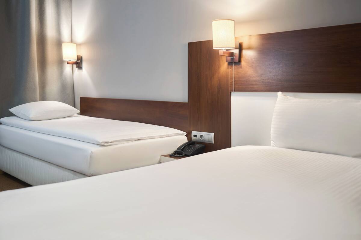 A hotel room with two beds, a wooden headboard, bedside lamps, a phone, and a curtain.