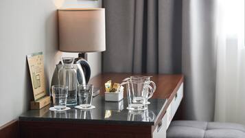 A hotel room with a desk, a lamp, a pitcher, glasses, and a sign.