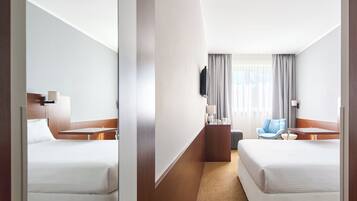 Een hotelkamer met twee bedden, een bureau, een stoel, een televisie en een raam met gordijnen.