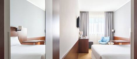 A hotel room with two beds, a desk, a chair, a TV, and a window with curtains.