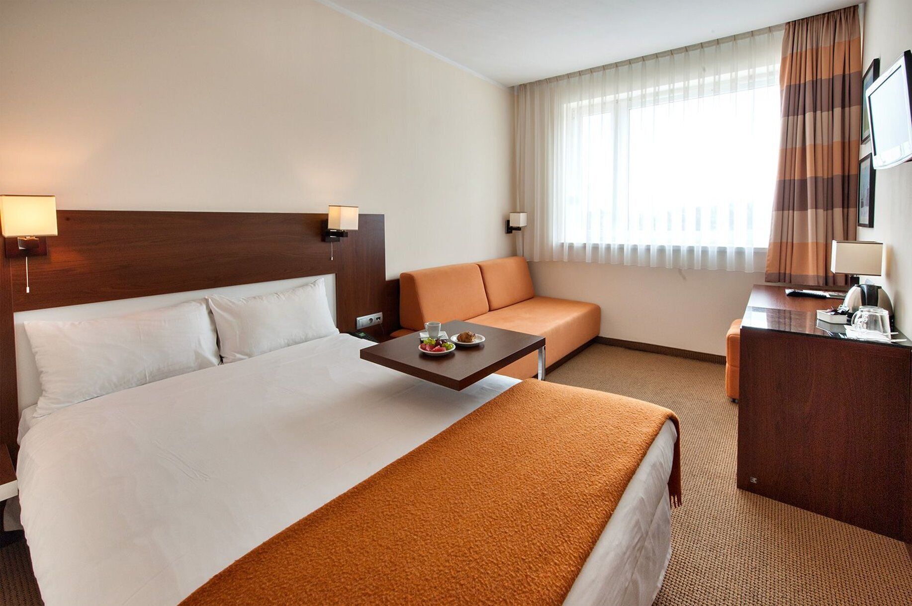 Una habitación de hotel con cama, sofá, escritorio y ventana con cortinas.