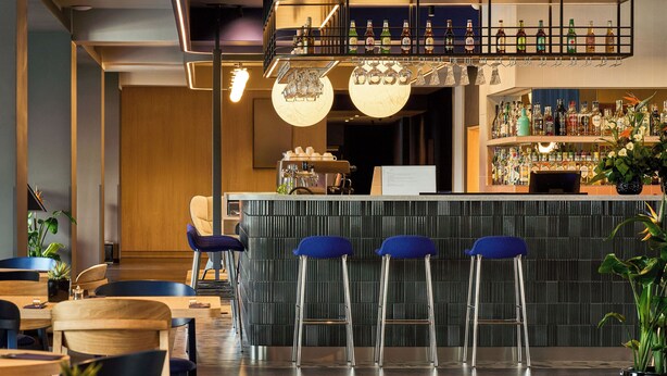 A bar area with stools, a counter, and a variety of bottles and glasses.
