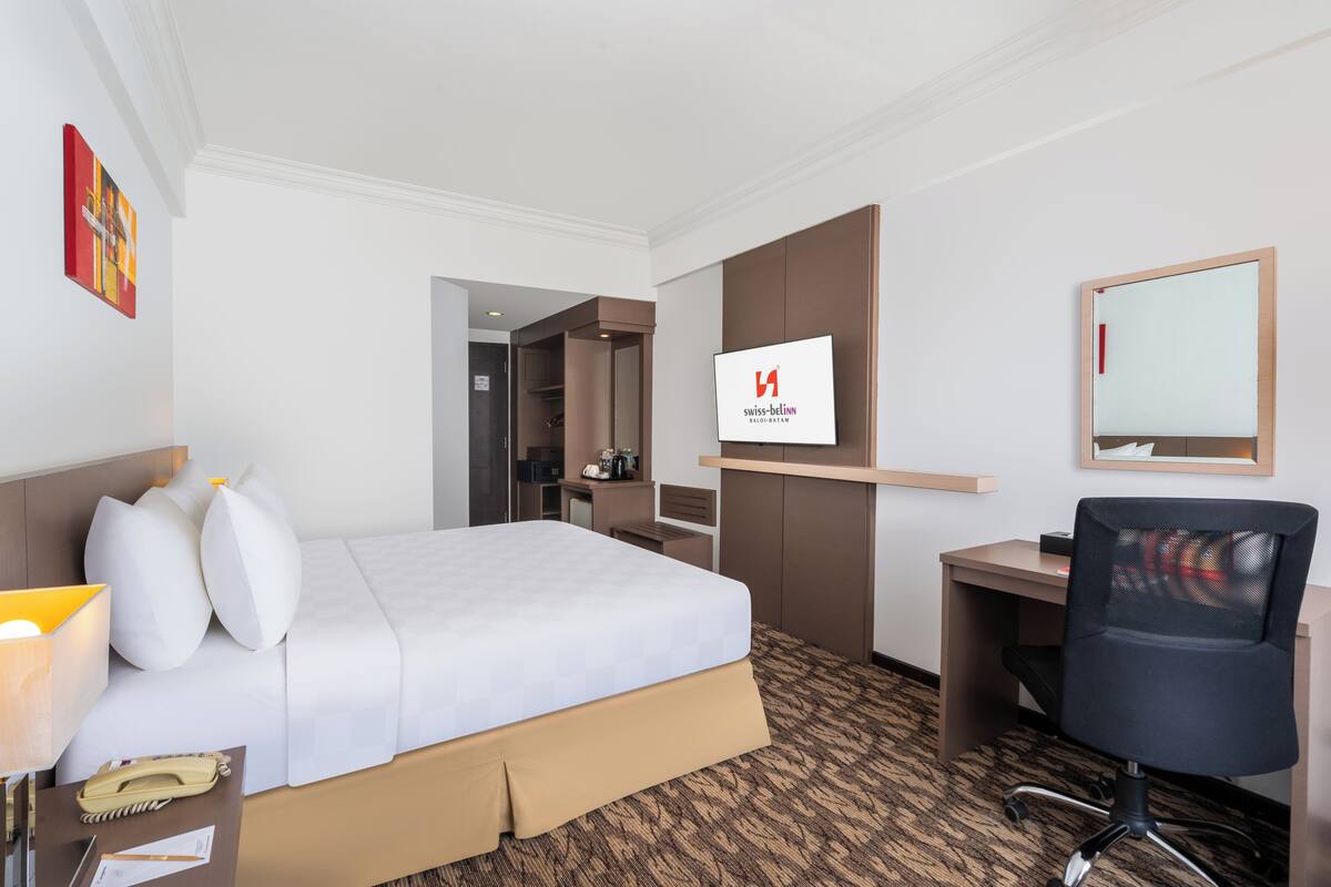 Une chambre d’hôtel équipée d’un lit, d’un bureau, d’une chaise et d’un écran fixé au mur sur lequel est affiché le nom de l’hôtel.