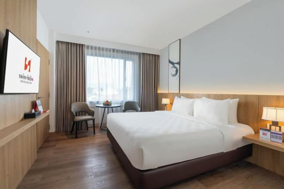 A hotel room with a large bed, a desk, a chair, a small table, and a TV mounted on the wall.