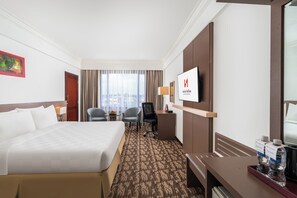 A hotel room with a large bed, a desk, two chairs, a TV, and a window with curtains.