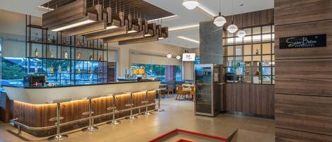 Un espace bar moderne avec un comptoir en bois, de nombreux tabourets et des luminaires suspendus.