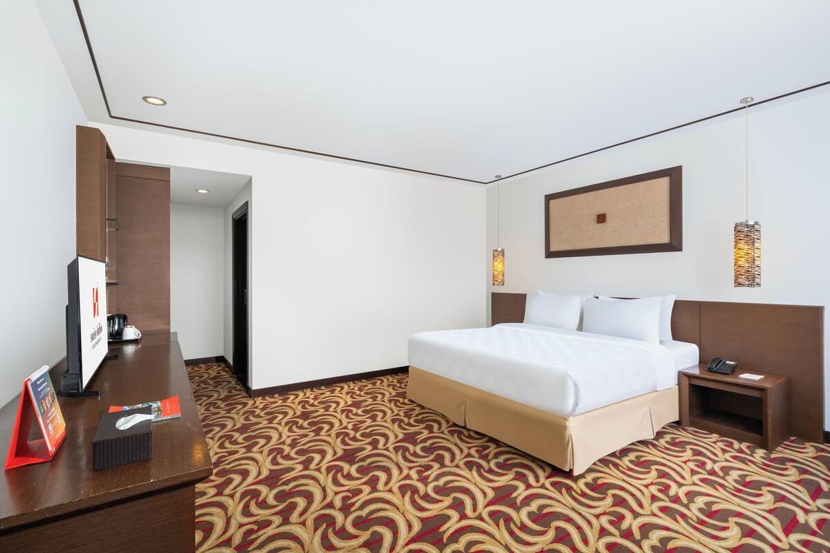 Une chambre d’hôtel avec un lit, un bureau équipé d’un ordinateur, un téléphone et un tableau accroché au mur.