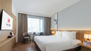 Una habitación de hotel con una cama grande, un escritorio, una silla, una mesita y un televisor en la pared.