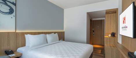 Una habitación de hotel moderna con una cama grande, una mesita de noche con teléfono, un televisor de pantalla plana y un armario de madera.