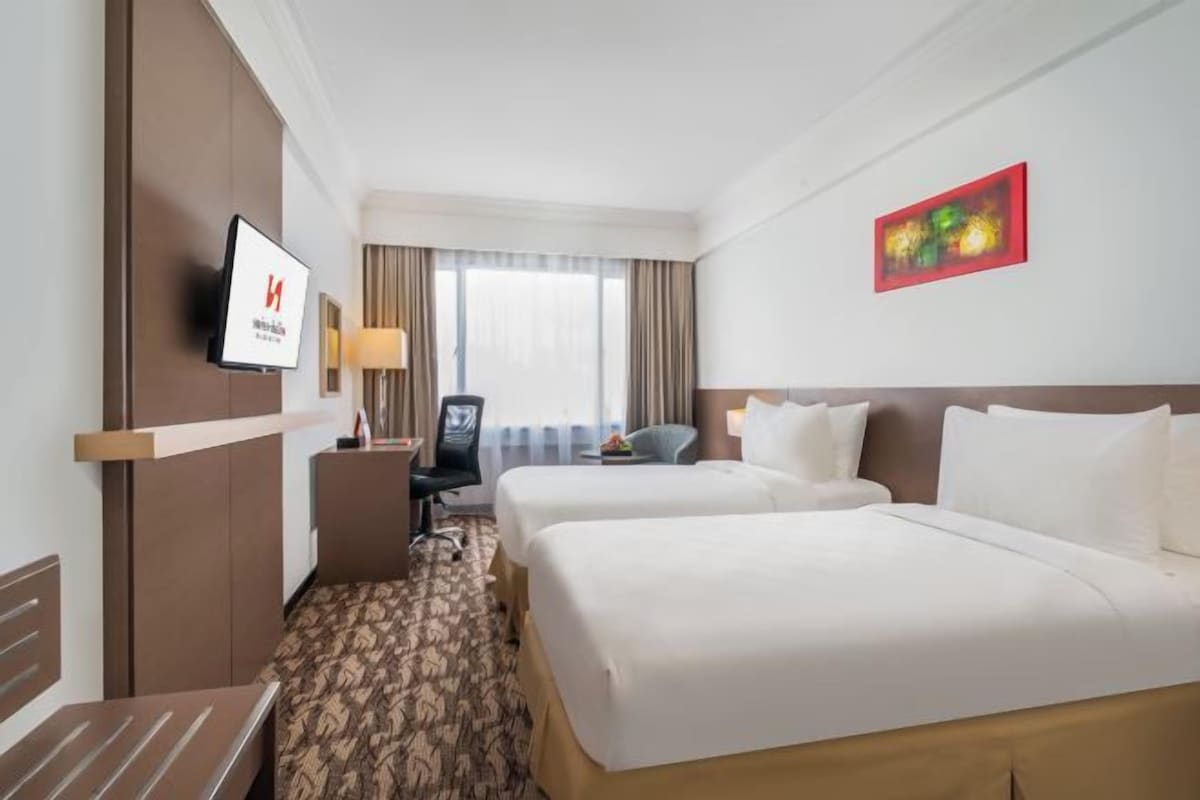 A hotel room with two beds, a desk, a chair, a TV, and a window with curtains.