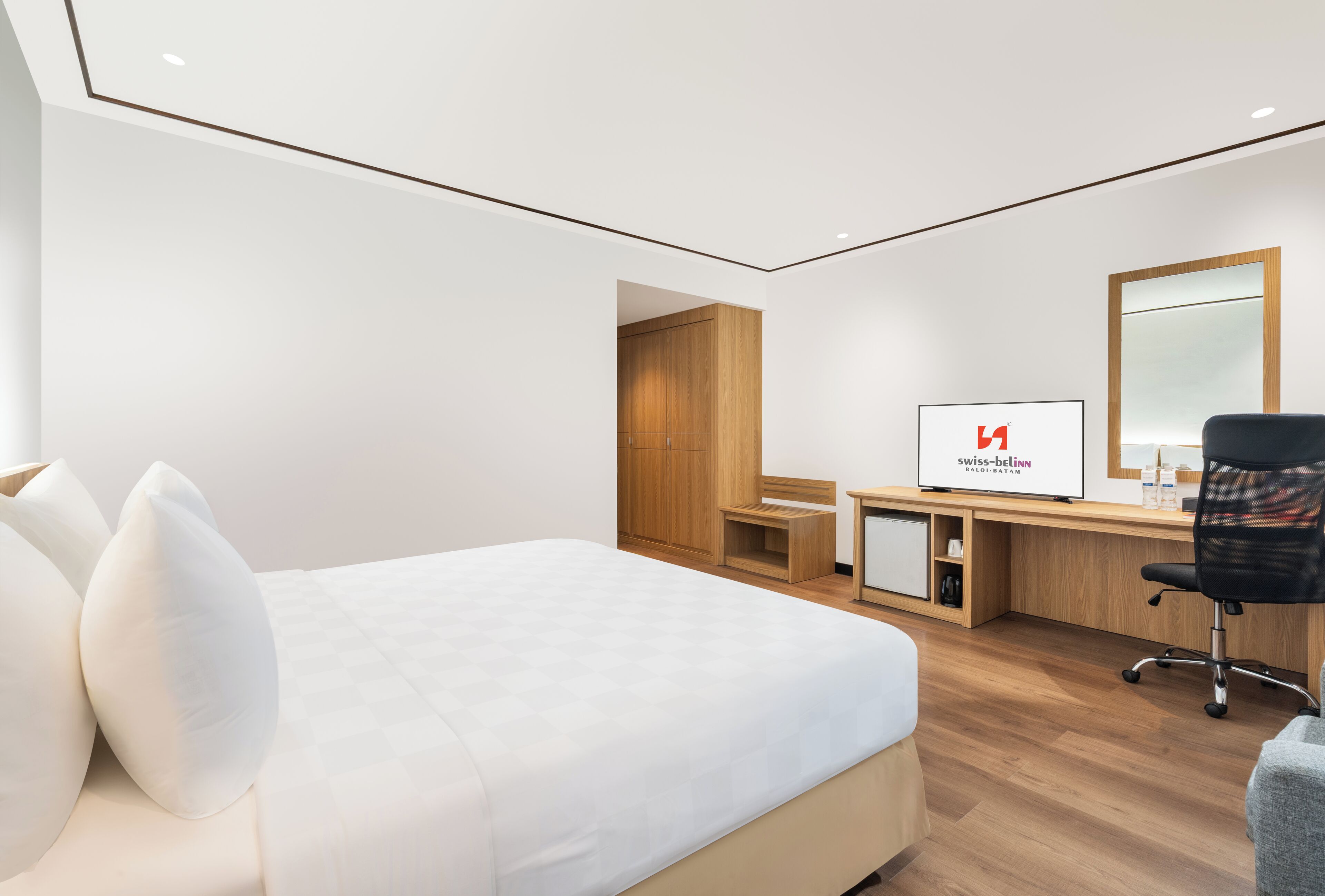 Et moderne hotelværelse med en stor seng, et skrivebord, en stol og et fjernsyn, der viser Swiss-Belgium logoet.