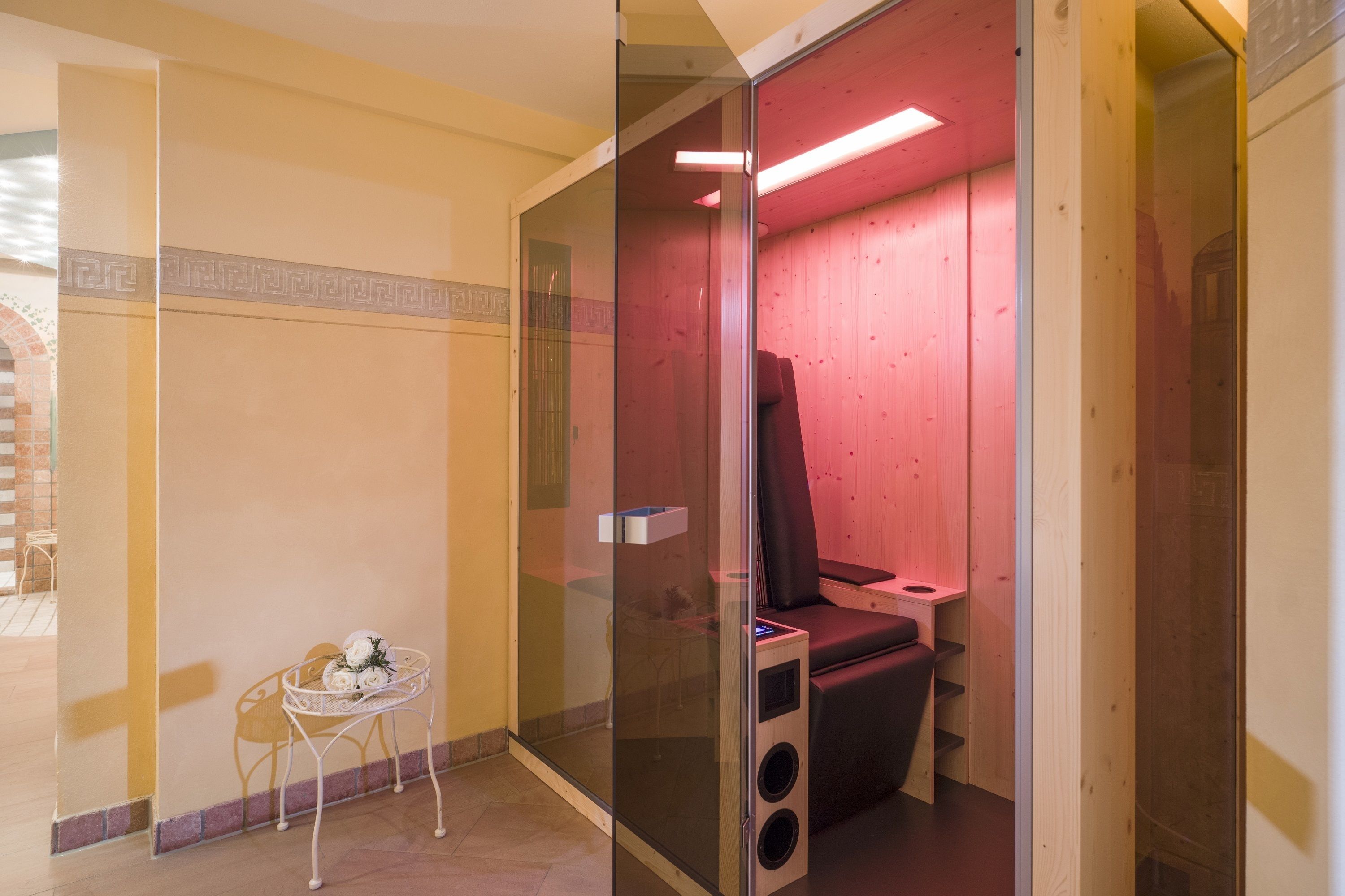 A sauna room with a glass partition, a wooden bench, and a small table with a vase of flowers.