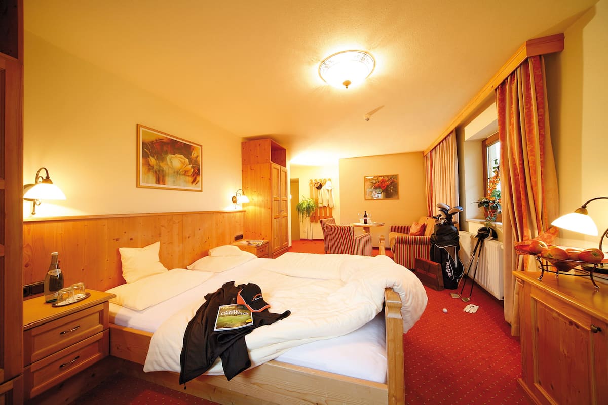 A hotel room with a large bed, a desk with a lamp, a chair, and a coat rack.